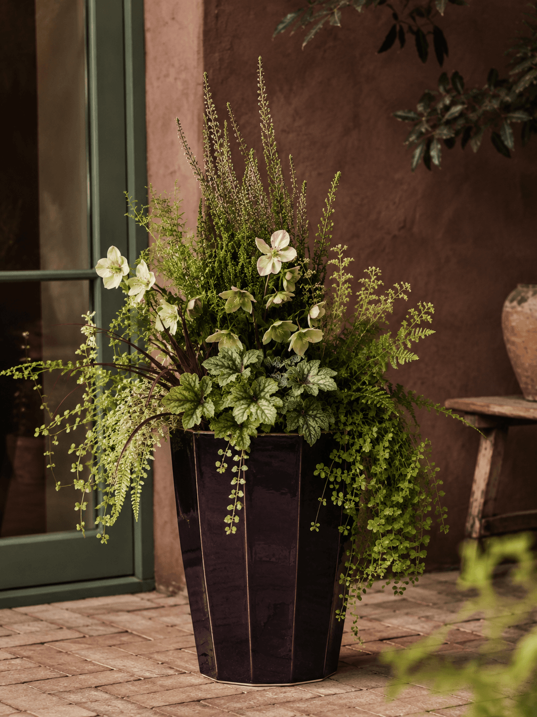 A burgundy planter with white flowers on a garden potting bench